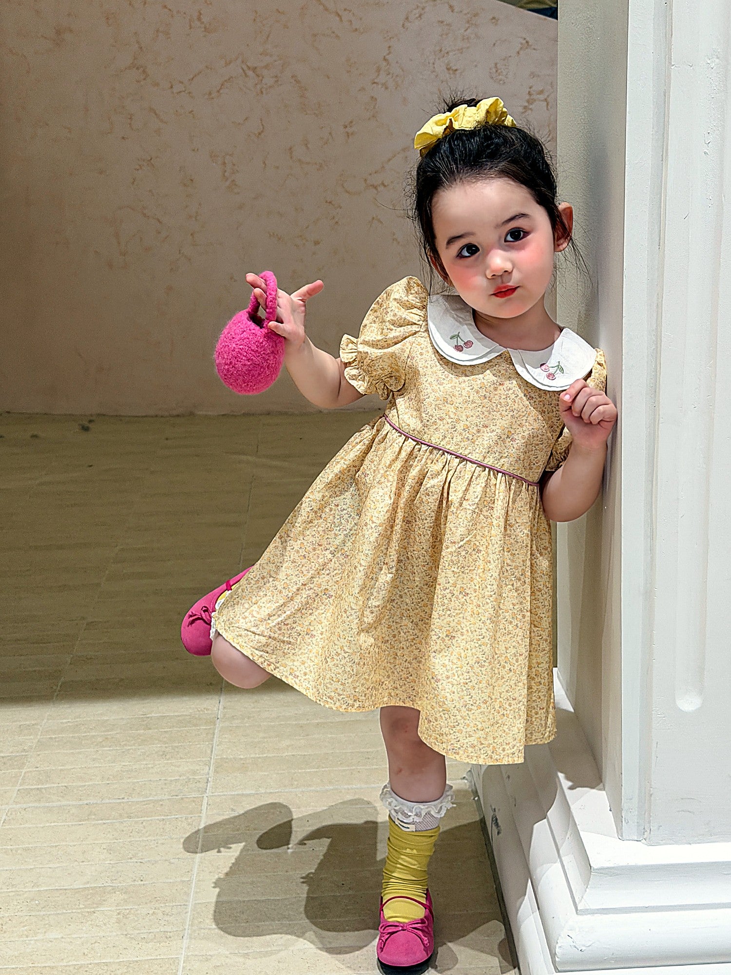 A young girl in a butter-yellow cotton dress with a white embroidered collar.