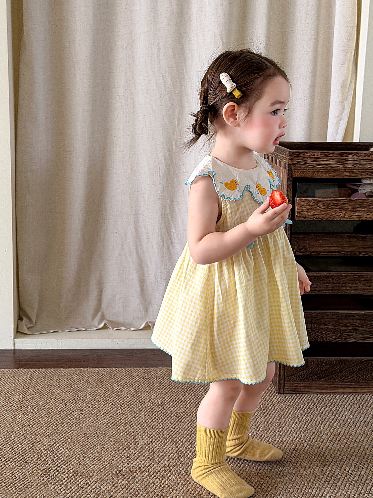 A young girl in a butter-yellow gingham pinafore with a white embroidered collar.