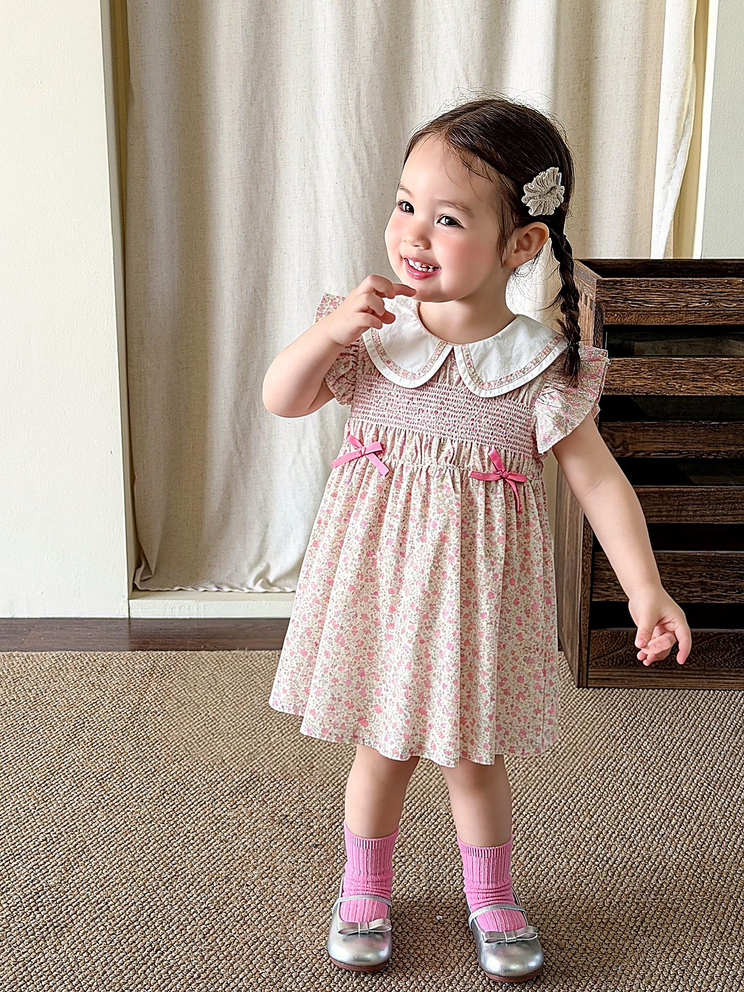 A young girl in a warm-pink cotton dress with a lace collar and puff sleeves.