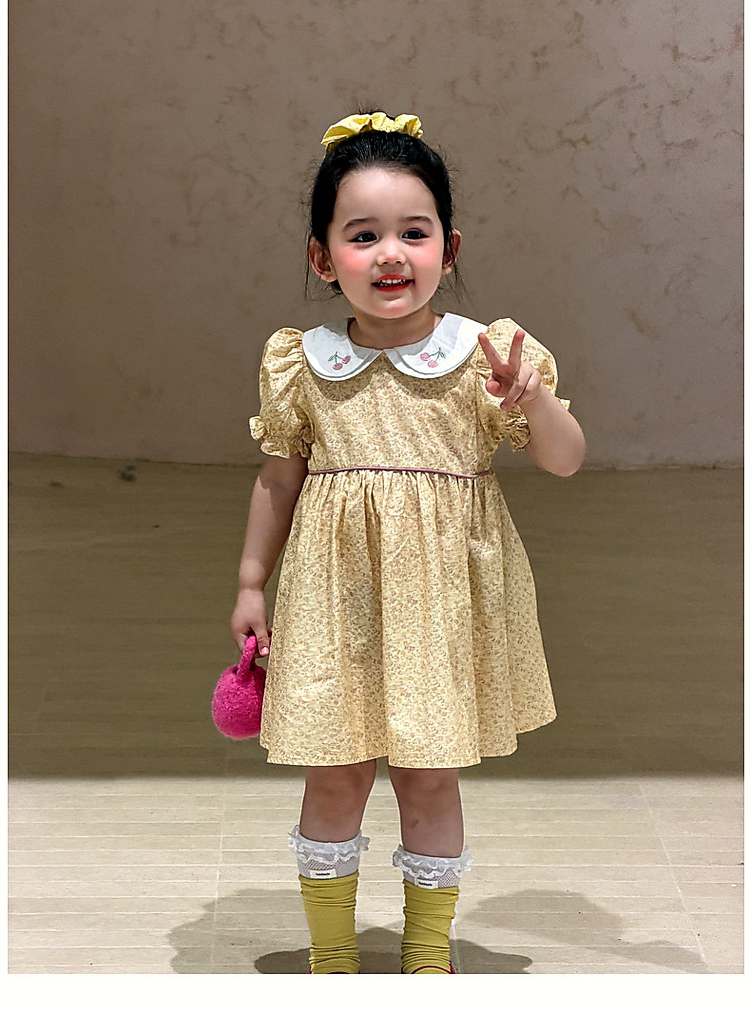 A toddler in the Cowslip Dress with spring flowers, soft light.