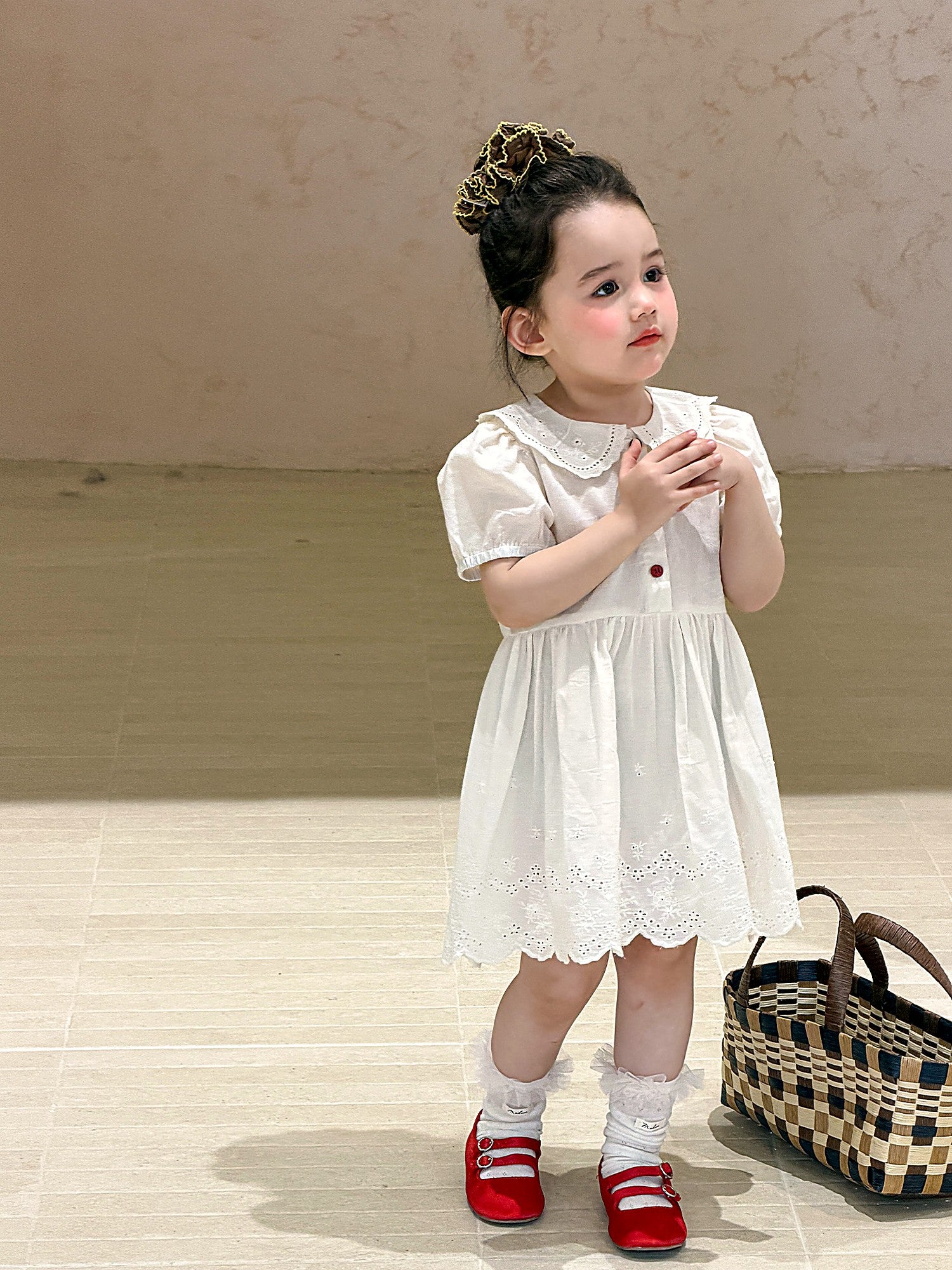 A young girl in an ivory eyelet cotton dress with a lace collar.
