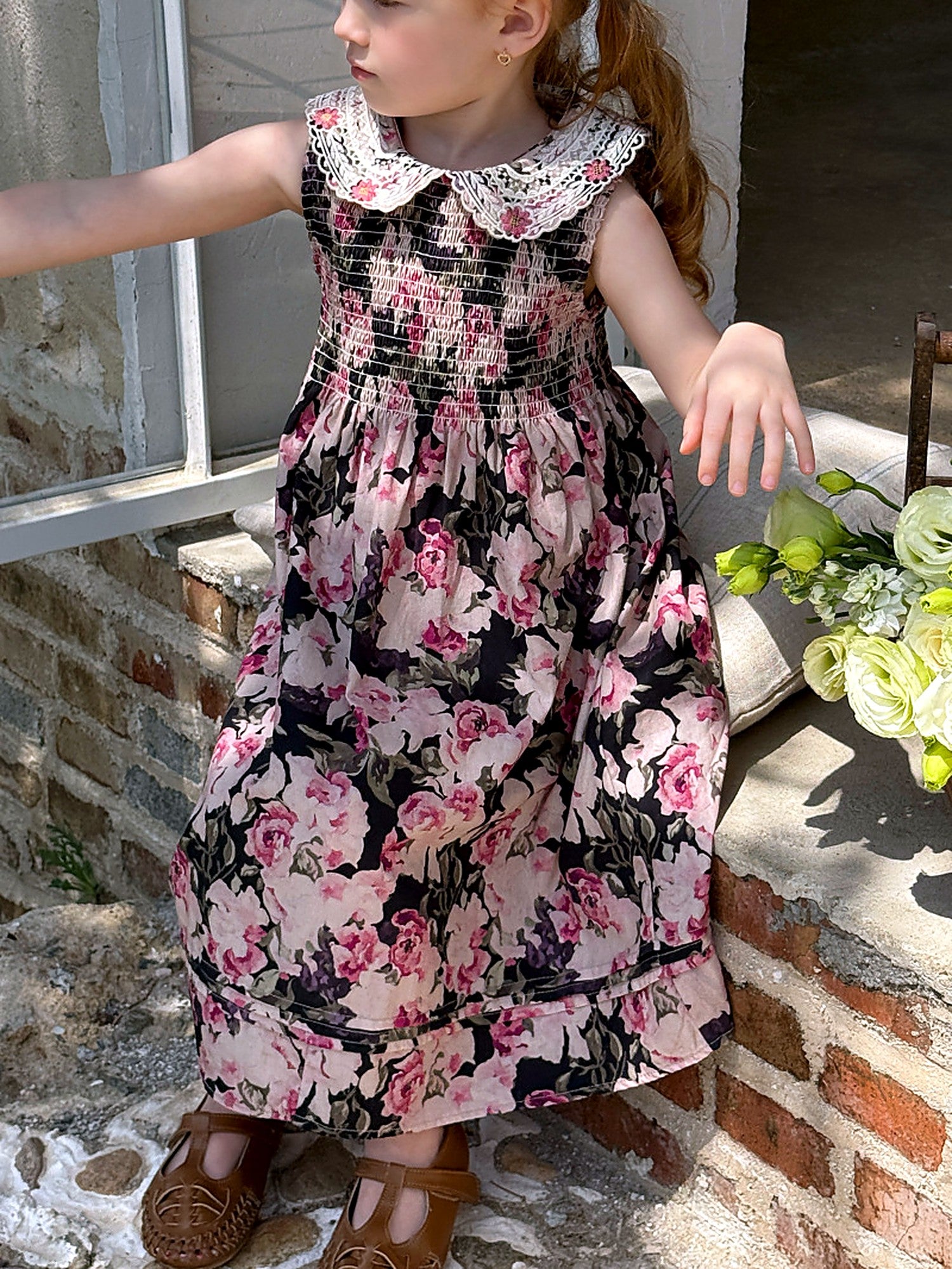 A girl in a dark floral cotton maxi dress with a lace collar, in a sunlit garden.