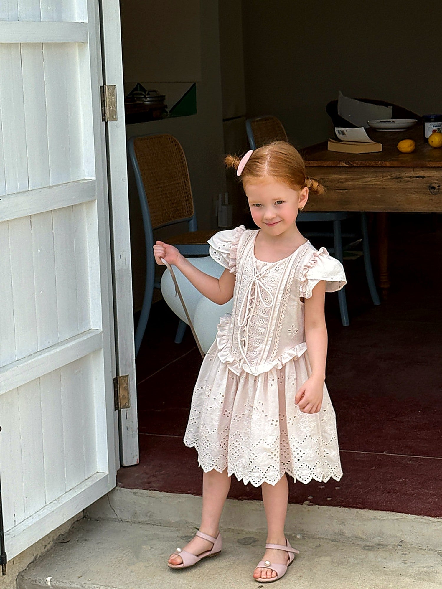 A girl in the Mallow Dress in a rustic doorway, dressed for a summer party.