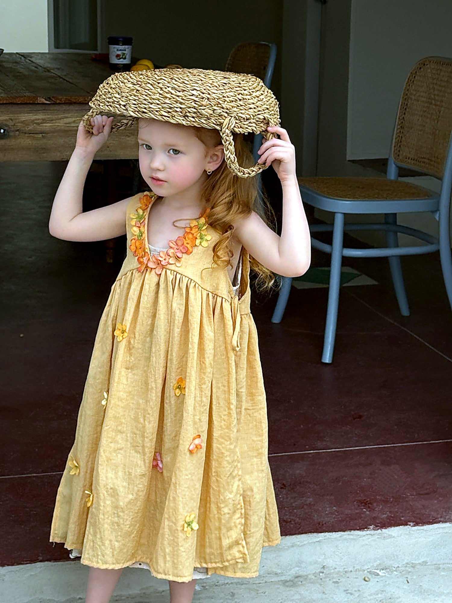 A girl in a marigold-yellow cotton dress with a gathered tiered skirt, in a sunlit vintage room.