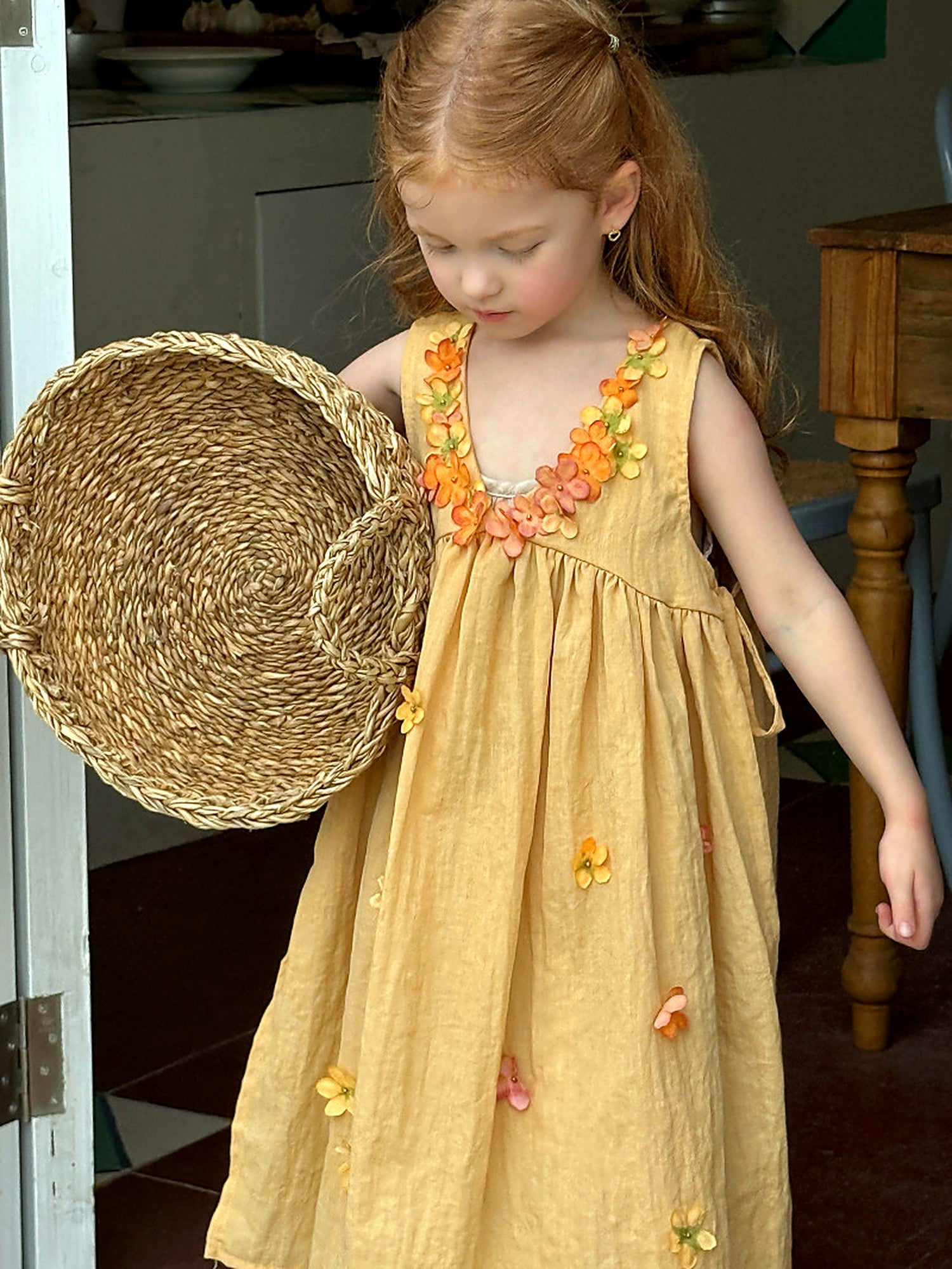 A girl in the Marigold Dress by a window, baskets and soft afternoon light.