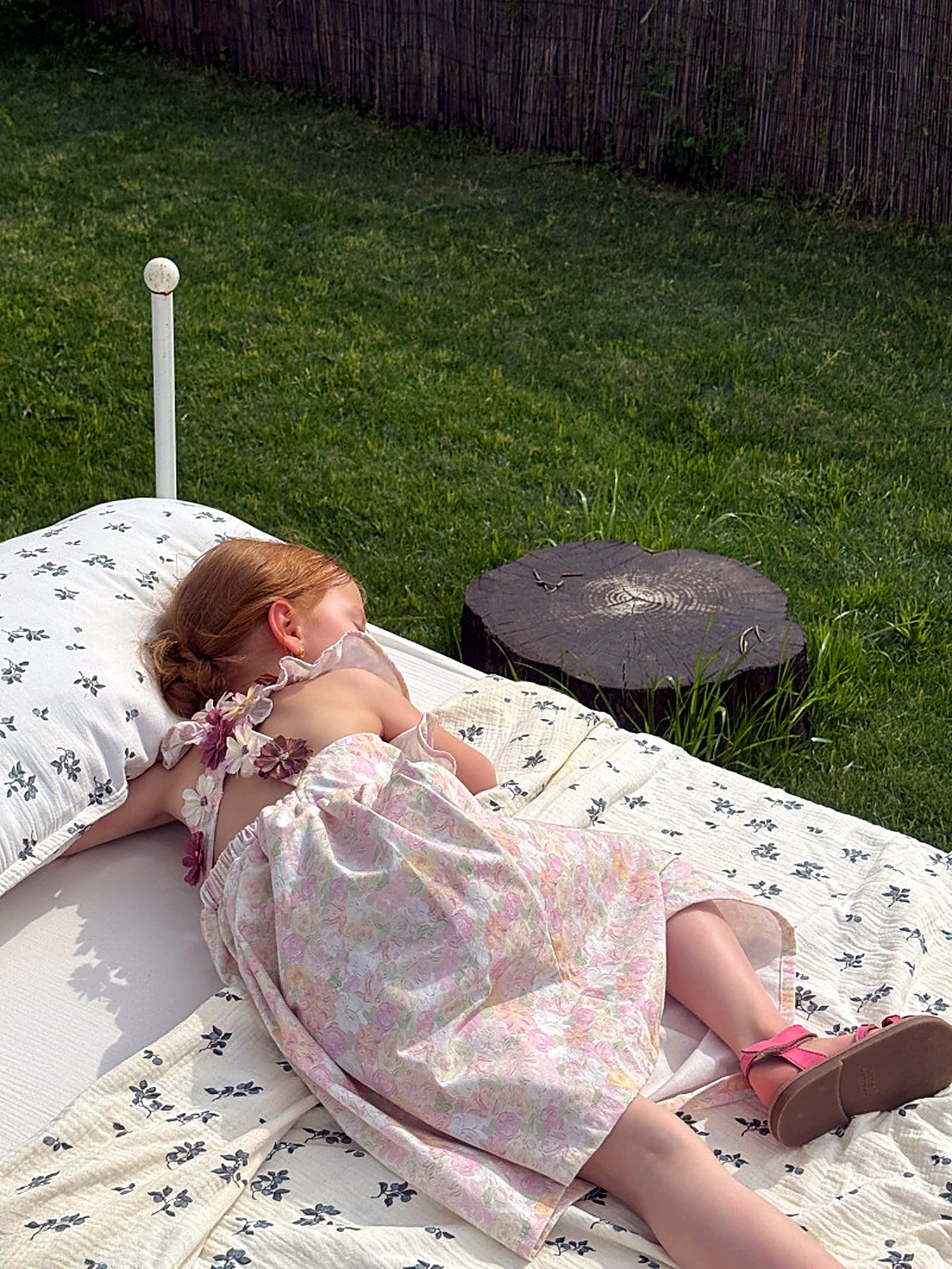 The low, tied open back of the Peony Dress, seen in a garden beside a wooden ladder.