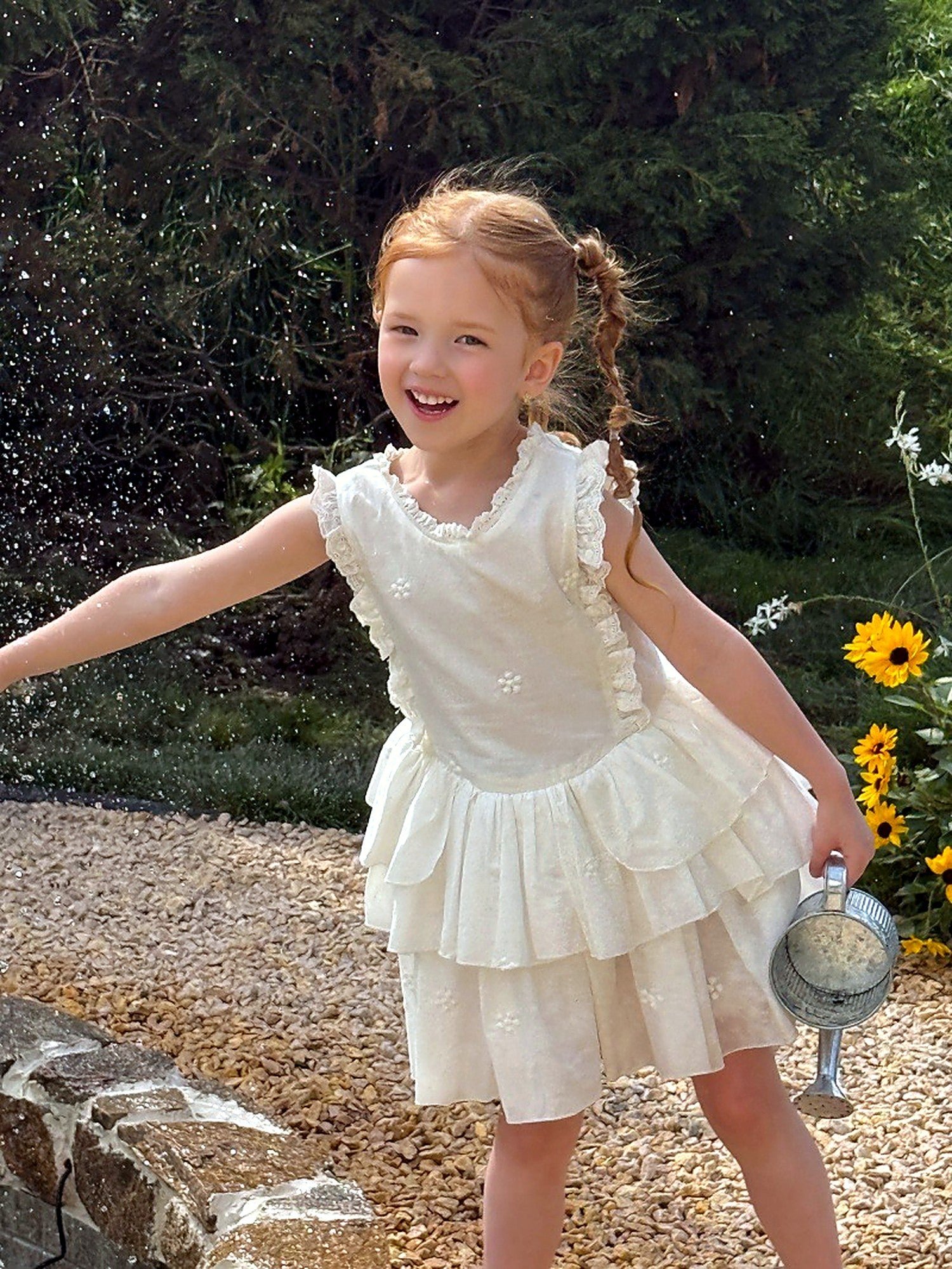 A girl in an ivory cotton dress in tiers of ruffle and lace, in a sunlit garden.